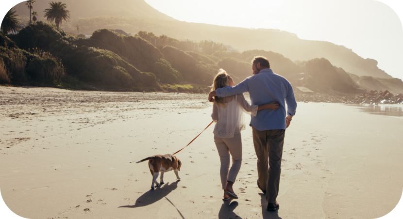 Couple walking on the beach with a dog and after reviewing their health insurance plan.